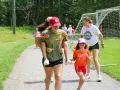 Mädchen haben Spaß bei einem Sommercamp in den USA. Eine trägt die andere auf dem Rücken, während sie lachend über einen Weg laufen.