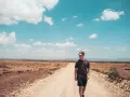 Ein junger Mann mit Kappe geht auf einer staubigen Straße in der afrikanischen Savanne. Ein bezahltes Praktikum im Ausland nach dem Abitur ist ein Abenteuer.