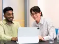 Ein junger Mann und eine Frau lachen über den Bildschirm eines Tablets. Sie sind bei einem Praktikum Studium und scheinen eine gute Zeit zu haben.