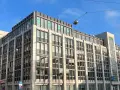 Modernes Bürogebäude in Kassel mit vielen Fenstern und "FOM"-Logos. Eine Apotheke ist im Erdgeschoss sichtbar.