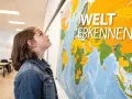 Ein Mädchen blickt auf eine Weltkarte mit der Aufschrift "Welt erkennen". Vielleicht plant sie ihren nächsten schuljahr im ausland.