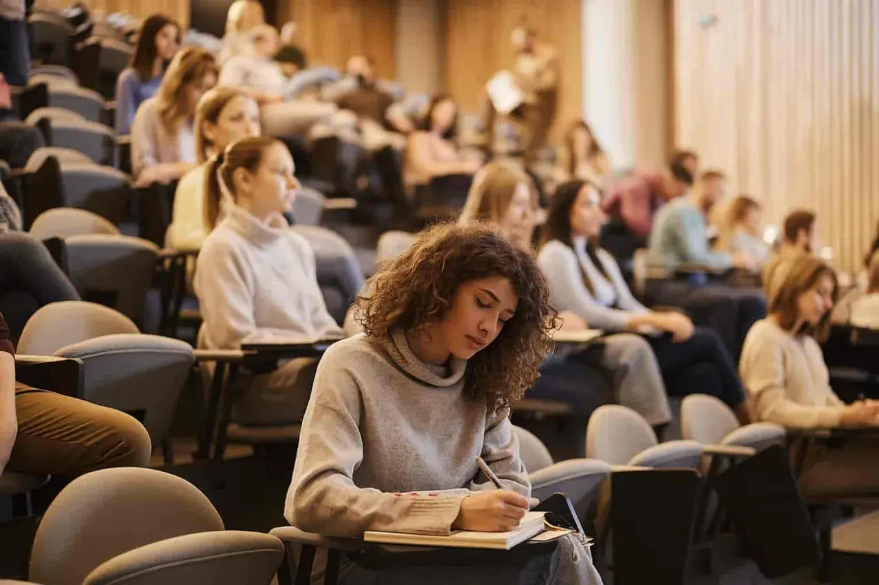 Junge Frau mit Locken schreibt konzentriert in ein Notizbuch, während sie an ihrem Erasmus Studium teilnimmt.