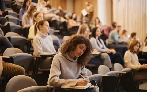 Junge Frau mit Locken schreibt konzentriert in ein Notizbuch, während sie an ihrem Erasmus Studium teilnimmt.