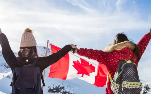 Zwei junge Frauen mit Rucksäcken und der kanadischen Flagge in den Bergen. Ein unvergesslicher Kanada Austausch!