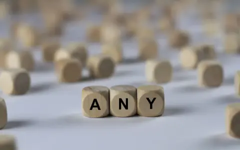 Holzwürfel mit den Buchstaben A, N, Y bilden das Wort "ANY". Sie liegen auf einem hellen Untergrund, umgeben von vielen weiteren unscharfen Würfeln.