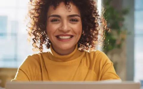 Lächelnde Frau mit Locken am Laptop, bereit für ihre Bewerbung als studentische Hilfskraft.