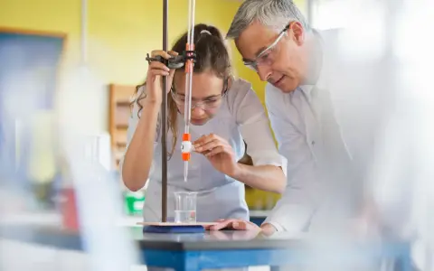 Schülerin bei chemischem Experiment mit Lehrer. Perfekt für die Ausbildung mit Abitur NRW.