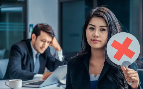 Frau hält rotes Kreuz, lehnt eine Ausbildung zur oder als ab. Mann im Hintergrund wirkt frustriert.