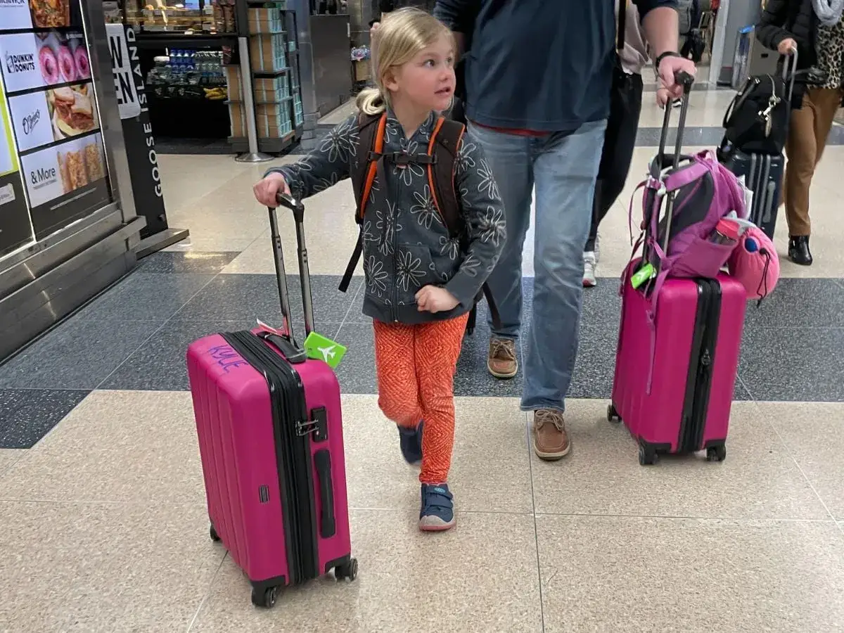 Ein kleines Mädchen mit einem Rucksack und einem pinken Koffer, bereit für eine