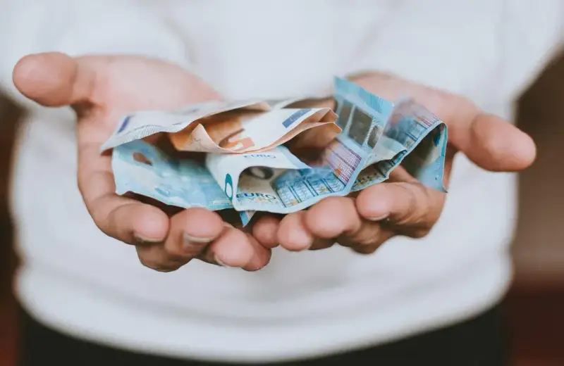 Hände halten zerknitterte Euro-Scheine. Das Geld ist für das geplante **auslandsjahr 3 monate** gedacht.
