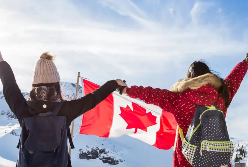 Zwei junge Frauen mit Rucksäcken und der kanadischen Flagge in den Bergen. Ein unvergesslicher Kanada Austausch!