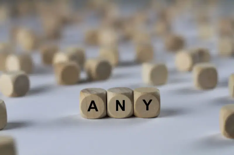 Holzwürfel mit den Buchstaben A, N, Y bilden das Wort "ANY". Sie liegen auf einem hellen Untergrund, umgeben von vielen weiteren unscharfen Würfeln.